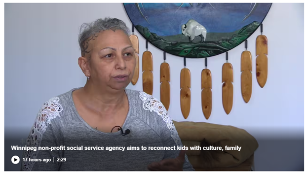 Cara Widrick seated in front of circular wood carving that has carved feathers hanging from it.